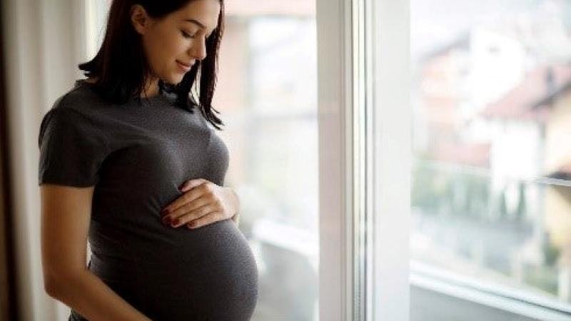 A pregnant women holding her belly while looking out of a window