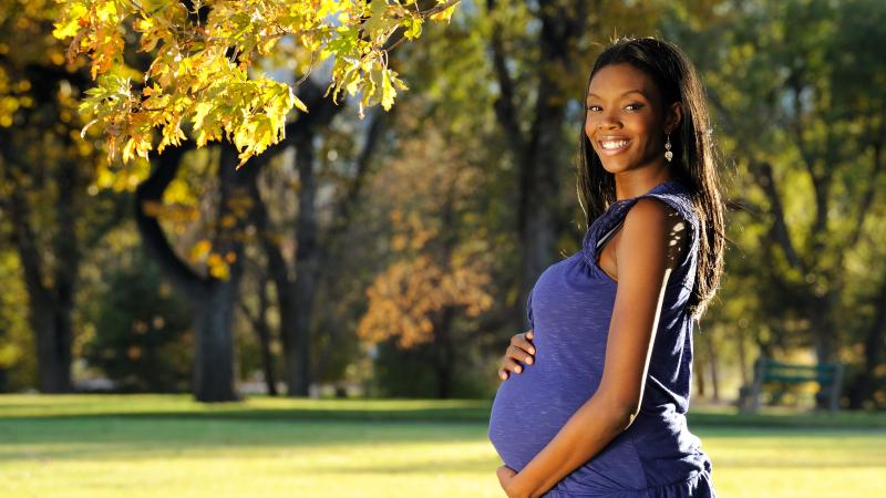 Pregnant woman standing outside holding her stomach 